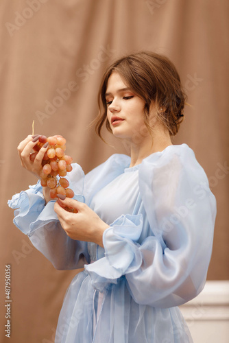 a girl in a blue dress with a bunch of grapes in her hands