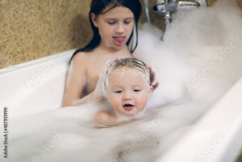 Cute sibling children bathe in a bubble bath together. Children in the bathroom. The concept of hygiene and education.