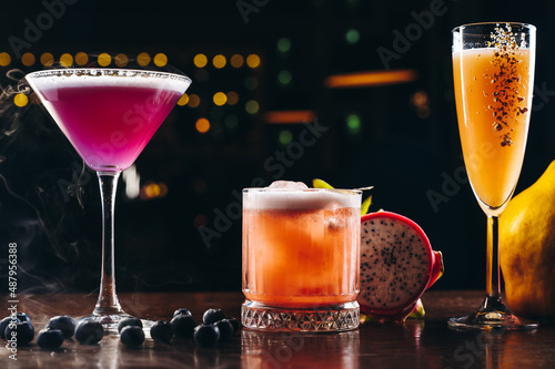 Three alcoholic cocktails, purple, orange and yellow colors on the table. Variety of colorful alcoholic drinks 