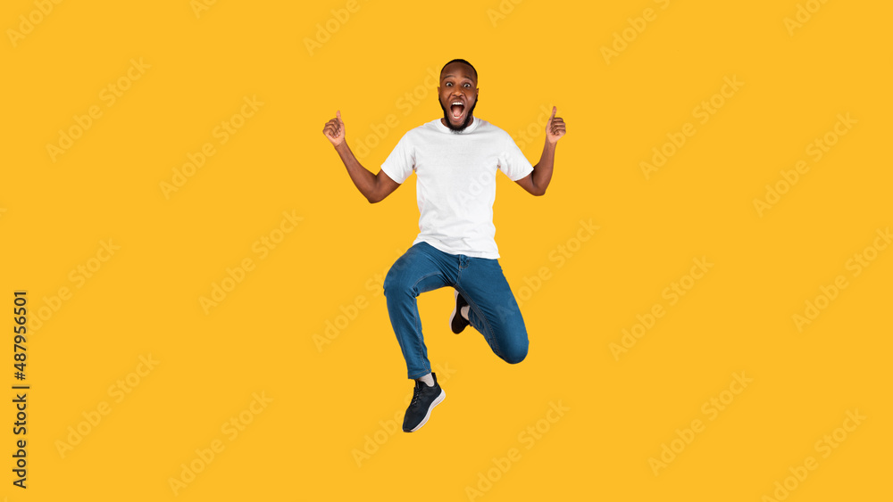 Excited African Man Gesturing Thumbs Up Jumping Over Yellow Background