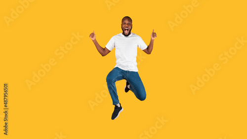 Excited African Man Gesturing Thumbs Up Jumping Over Yellow Background © Prostock-studio