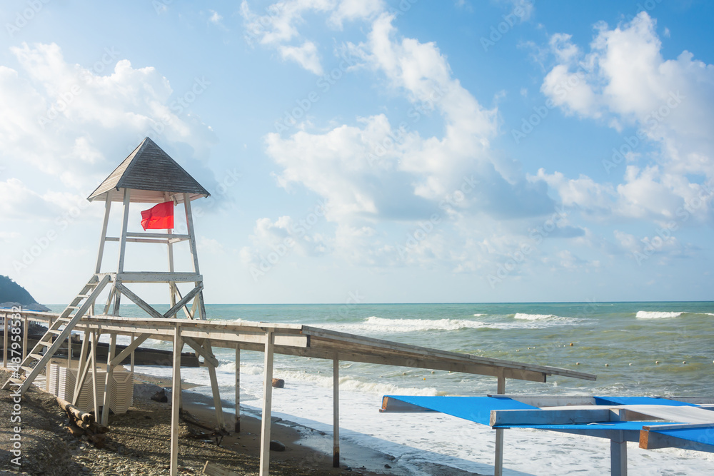 Red flag of danger on a rescue tower on the beach in summer. Stormy weather warning not to swim in the ocean or sea