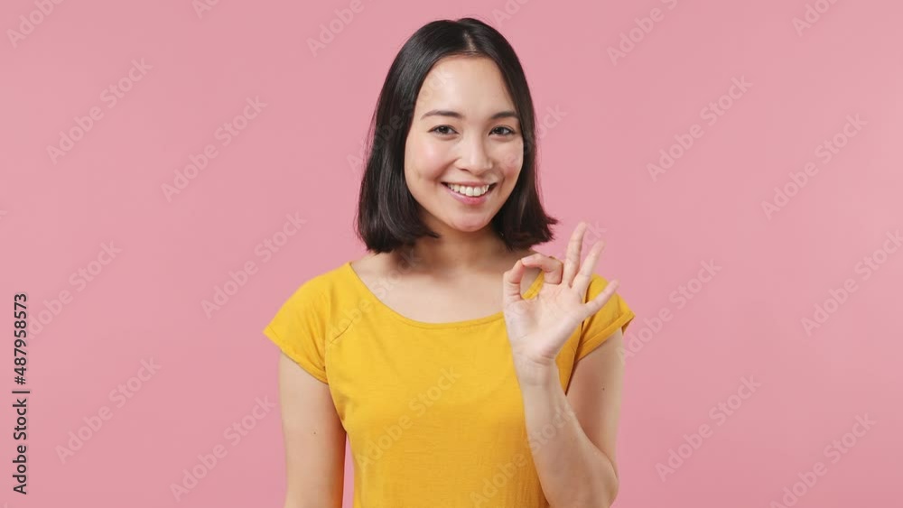 Cheerful young woman of Asian ethnicity 20s wears yellow t-shirt showing okay ok zero fingers gesture isolated on plain pastel light pink background studio portrait. People emotions lifestyle concept Cheerful young woman of Asian ethnicity 20s wears yellow t-shirt showing okay ok zero fingers gesture isolated on plain pastel light pink background studio portrait. People emotions lifestyle concept