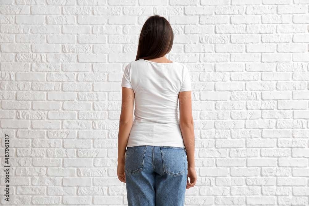 Young woman in blank t-shirt on white brick background, back view Young woman in blank t-shirt on white brick background, back view