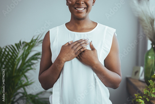 Portrait of happy millennial female volunteer holding folded hands on chest, looking at camera. Kind smiling young woman feeling thankful, showing appreciation, gratitude believe charity concept. photo