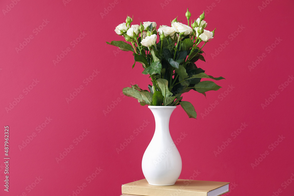 Vase with bouquet of beautiful fresh roses on book near red wall Vase with bouquet of beautiful fresh roses on book near red wall