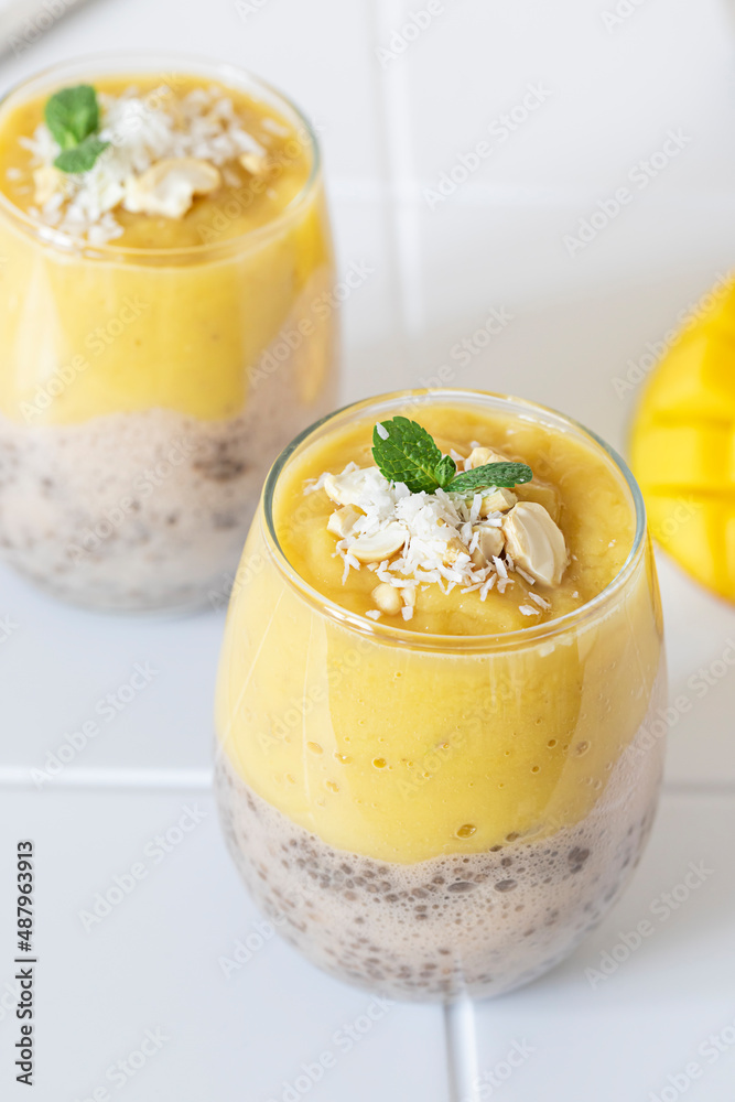 Delicious mango and chia pudding in a glass on the white ceramic tile table close up. Healthy morning breakfast concept Delicious mango and chia pudding in a glass on the white ceramic tile table close up. Healthy morning breakfast concept