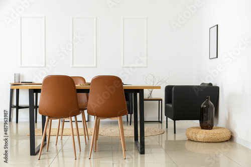 Interior of light dining room with table and black armchairs