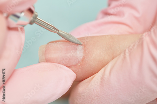Manicure treatment at nail salon. Removing the nail plate with a milling machine. Manicure process in beauty salon  cleaning of nails by a milling cutter. Shallow depth of field