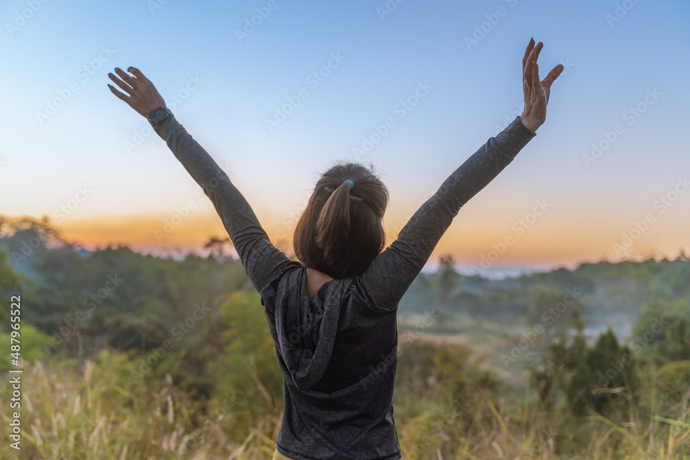 Beautiful young Asian woman in warm up jacket stretching her arms up during her break from her morning exercise run in a park Beautiful young Asian woman in warm up jacket stretching her arms up during her break from her morning exercise run in a park
