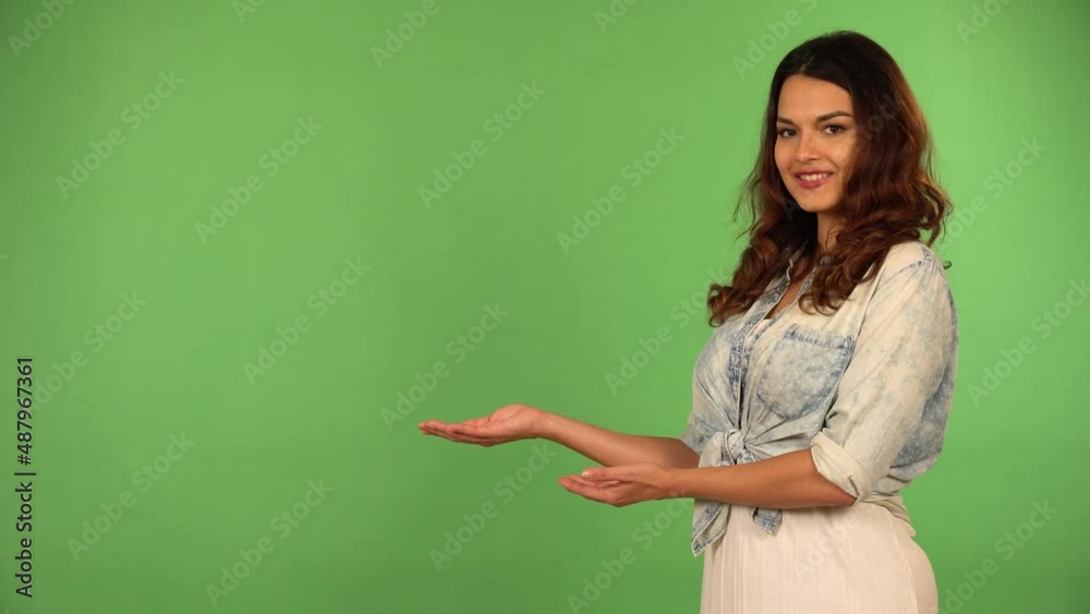 A young beautiful Caucasian woman presents something to the camera with a smile - green screen background A young beautiful Caucasian woman presents something to the camera with a smile - green screen background