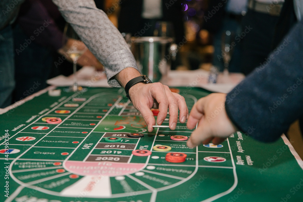 Close-up, hands of people playing in a wine casino, a man's hand with game chips on a green background of the table. Casino concept Close-up, hands of people playing in a wine casino, a man's hand with game chips on a green background of the table. Casino concept