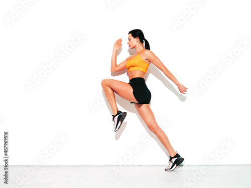 Fitness woman in sexy sports clothing. Young beautiful model with perfect body. Female posing in studio near white wall at summer sunny day. Jumping and running
