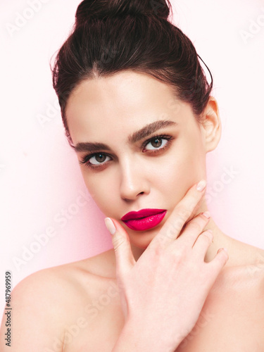 Fashion beauty portrait of young brunette woman with evening stylish makeup and perfect clean skin. Sexy model with hair in a bun posing in studio near white wall. With pink bright natural lips