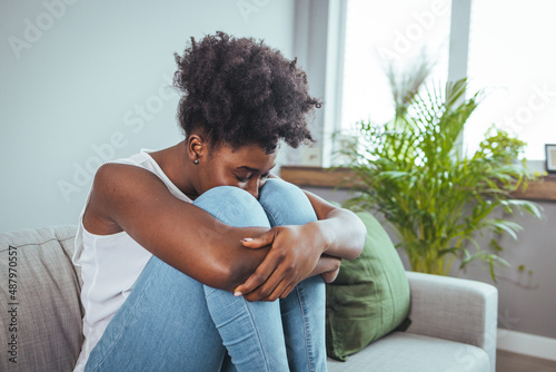 Side view young woman looking away at window sitting on couch at home. Frustrated confused female feels unhappy problem in personal life quarrel break up with boyfriend or unexpected pregnancy concept