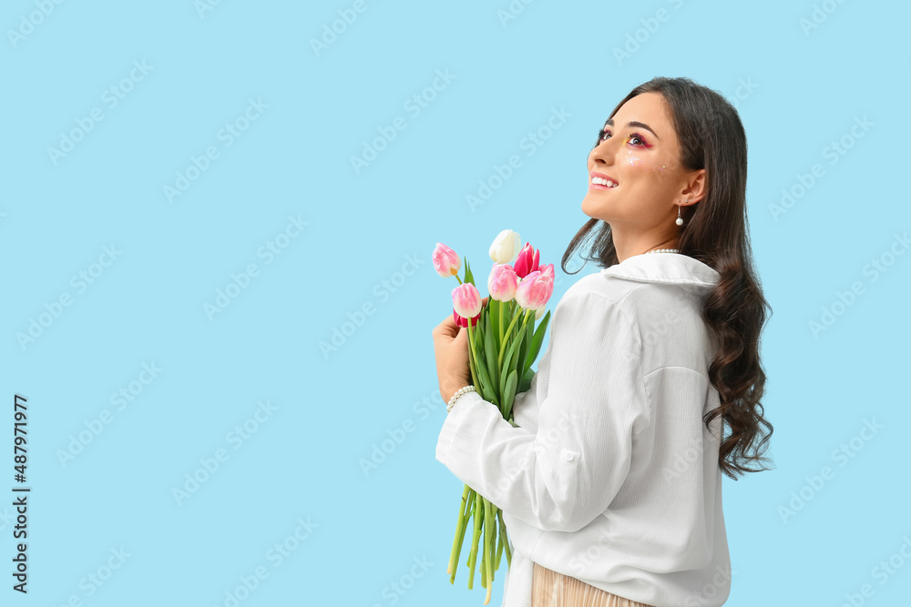 Fashionable woman with creative makeup holding bouquet of tulips on blue background. International Women's Day Fashionable woman with creative makeup holding bouquet of tulips on blue background. International Women's Day
