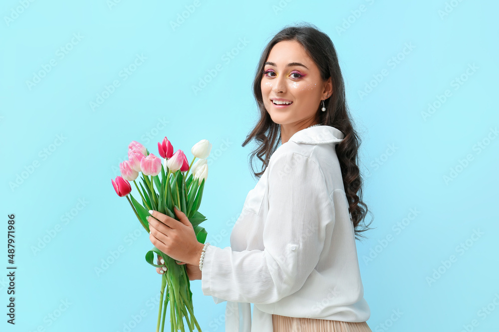 Elegant woman with creative makeup holding bouquet of tulips on blue background. International Women's Day Elegant woman with creative makeup holding bouquet of tulips on blue background. International Women's Day