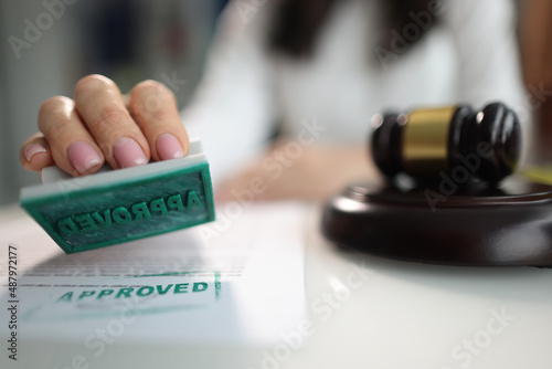 Hand puts stamp approved on document near judge's gavel