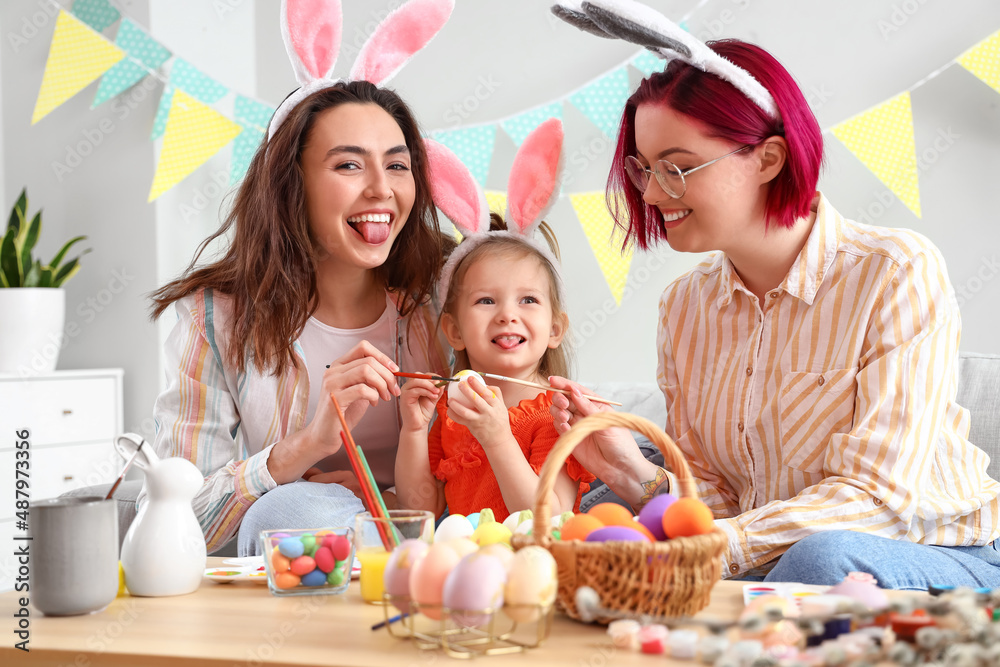 Young lesbian couple with little daughter having fun while painting Easter eggs at home Young lesbian couple with little daughter having fun while painting Easter eggs at home