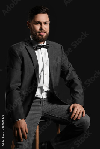 Stylish bearded man sitting on chair against dark background