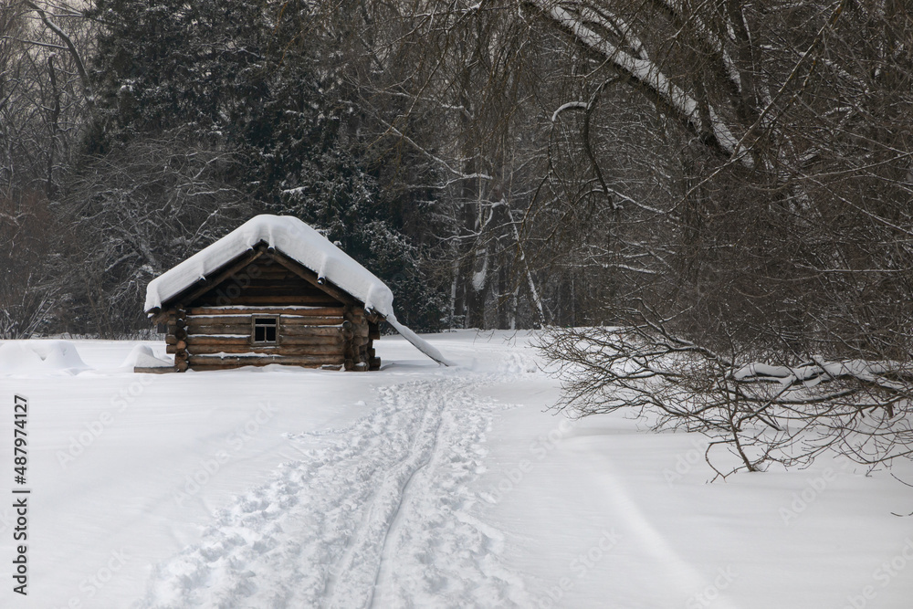 A lonely small rustic log house stands in the middle of the woods and snow drifts. There is a thick layer of snow on the roof of the house. A lot of snow and snow-covered trees all around. A lonely small rustic log house stands in the middle of the woods and snow drifts. There is a thick layer of snow on the roof of the house. A lot of snow and snow-covered trees all around.