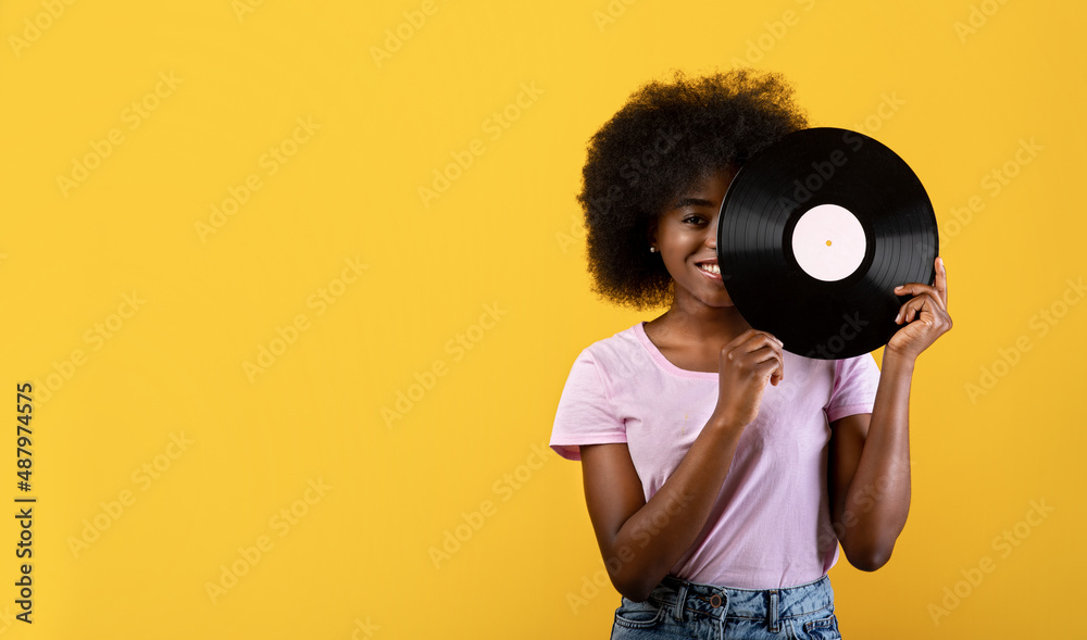 Fototapeta premium Retro music concept. Excited african american lady holding vinyl record and smiling on yellow background, panorama