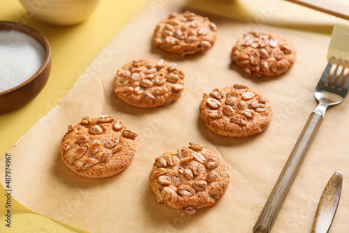 Parchment paper with tasty peanut cookies on yellow background