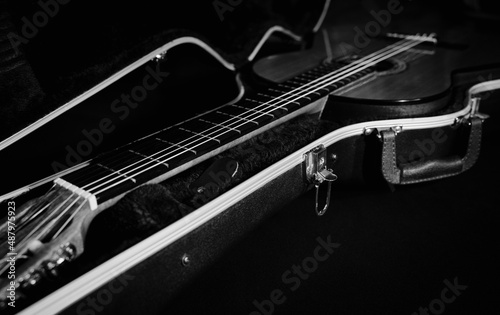 Black and white photo with a classical guitar in an open trunk. A black open trunk on a dark background with a flamenco guitar. Guitar neck.