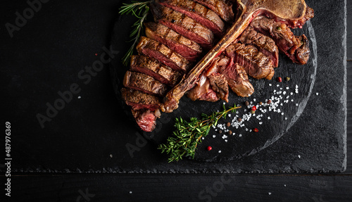 Barbecue dry aged wagyu porterhouse beef steak sliced with large fillet piece with hot chili as closeup on a modern design black cast iron tray