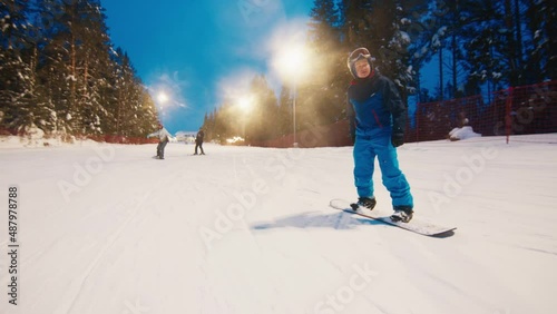 First time on snowboard. Woman learns snowboarding on the slope with her friends photo