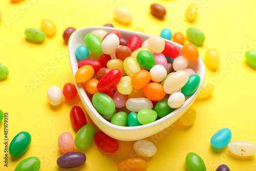 Bowl with different jelly beans on yellow background, closeup