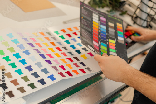 Cropped man hands choosing samples catalog palette rack color advertising T-shirts palette film membrane. Close up