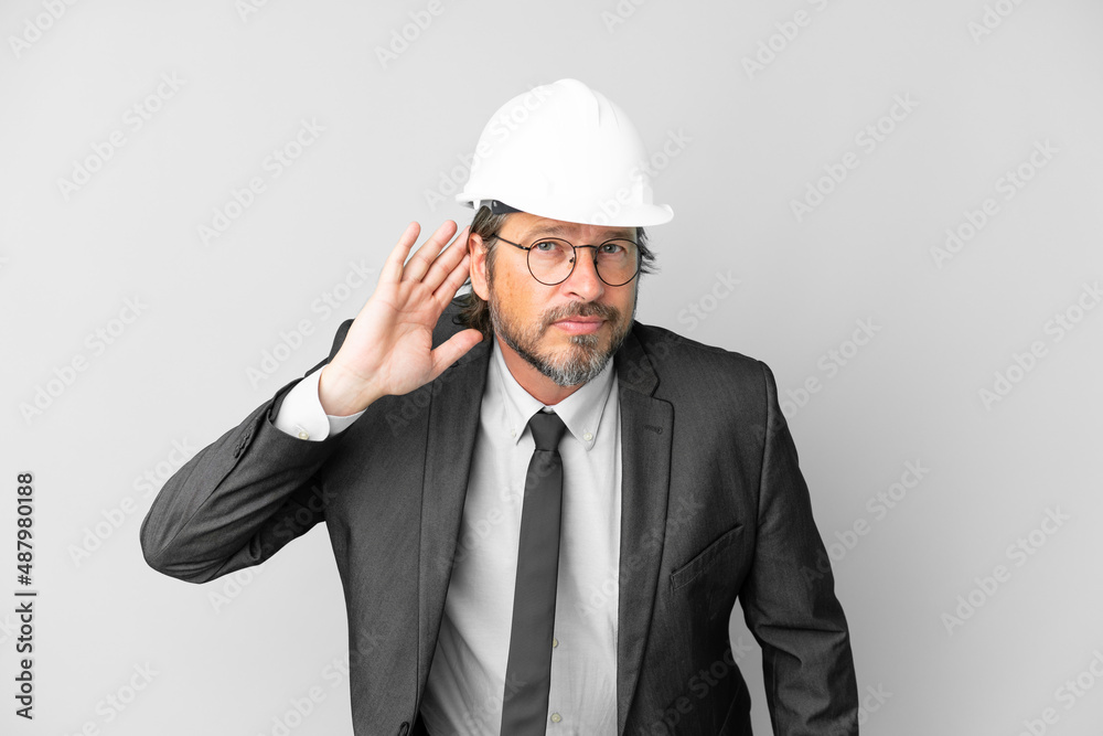 Young architect man with helmet over isolated background listening to something by putting hand on the ear Young architect man with helmet over isolated background listening to something by putting hand on the ear