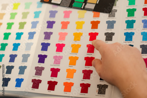 Cropped man hand choosing samples templates multicolor advertising T-shirts palette film membrane. Textile production photo
