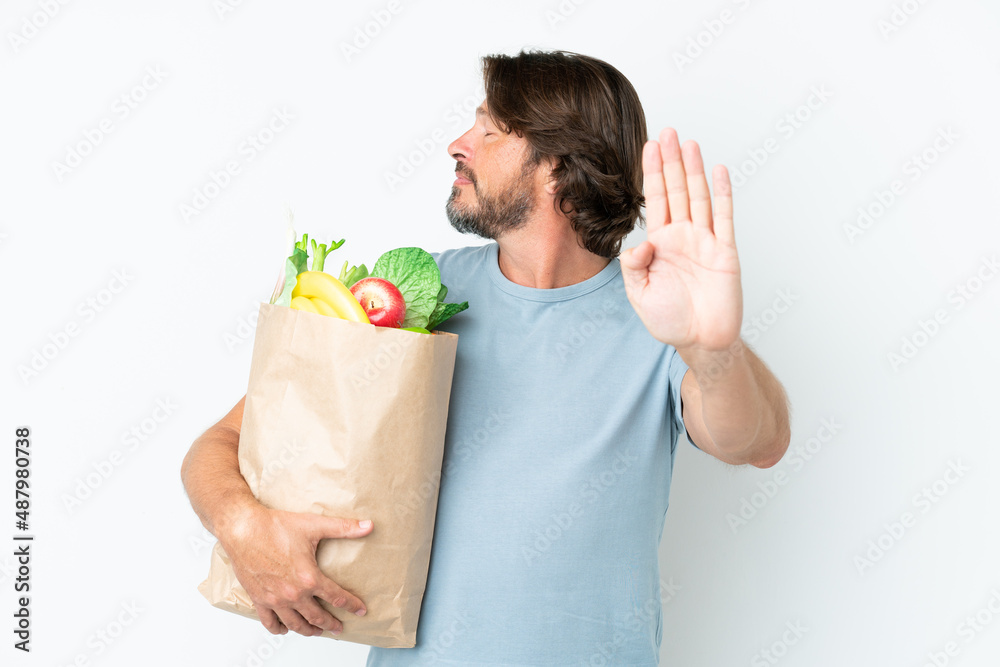 Senior dutch man holding grocery shopping bag over isolated background making stop gesture and disappointed Senior dutch man holding grocery shopping bag over isolated background making stop gesture and disappointed
