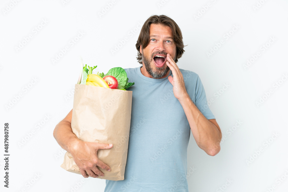 Senior dutch man holding grocery shopping bag over isolated background with surprise and shocked facial expression Senior dutch man holding grocery shopping bag over isolated background with surprise and shocked facial expression