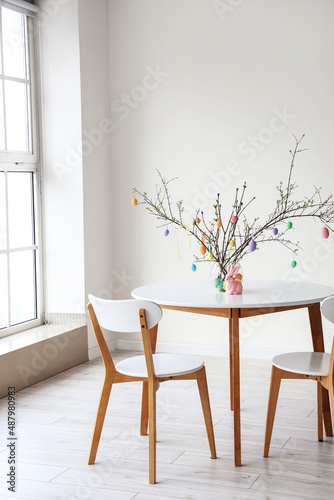 Fotografia Tree branches decorated with Easter eggs in vase and rabbit on dining table in l
