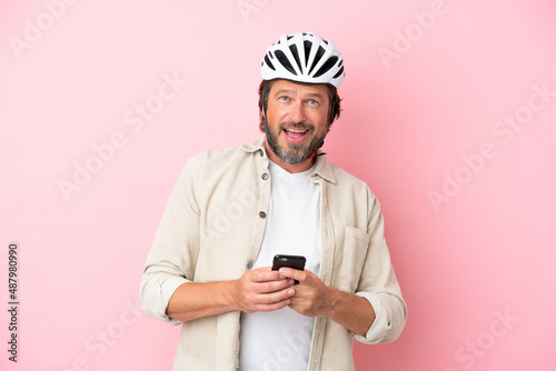Senior dutch man with bike helmet isolated on pink background surprised and sending a message