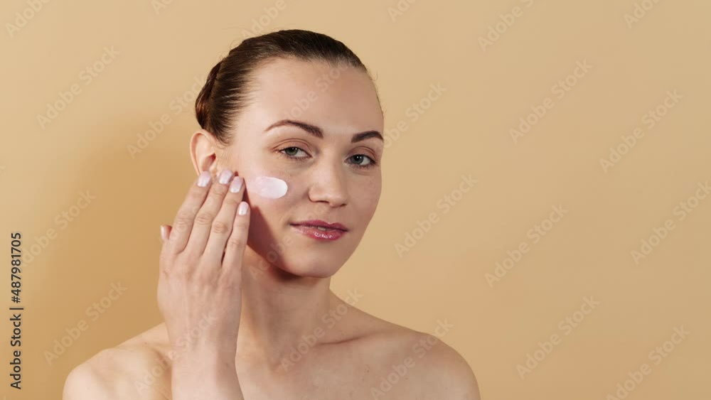 Attractive caucasian girl applying face cream on cheek isolated on beige studio background. Skin care concept. Attractive caucasian girl applying face cream on cheek isolated on beige studio background. Skin care concept.