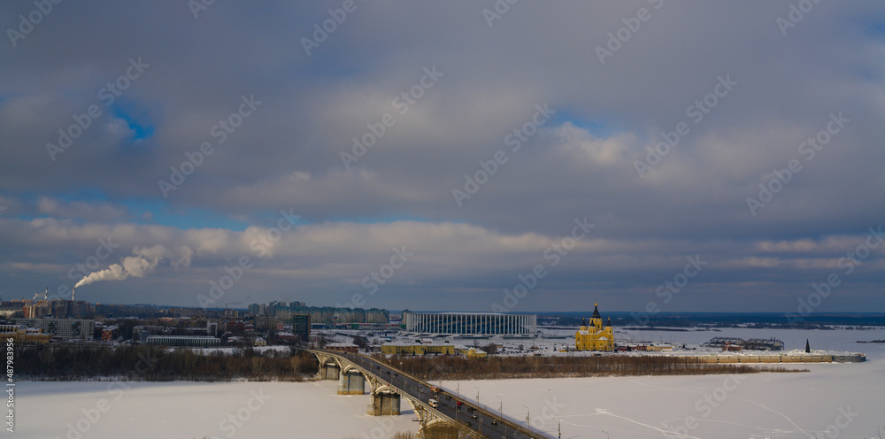 The landscape of a snow-covered northern city. A frozen wide river and a road bridge over it in a winter urban landscape.