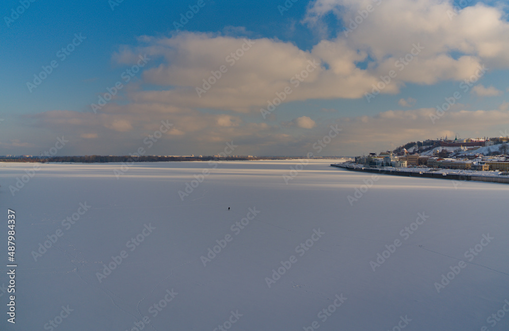 Panorama of the confluence of two large rivers. The snow-covered expanse of the mouth of a frozen river. Landscape of urban expanses with ancient city buildings. A fisherman on a winter fishing trip w Panorama of the confluence of two large rivers. The snow-covered expanse of the mouth of a frozen river. Landscape of urban expanses with ancient city buildings. A fisherman on a winter fishing trip w