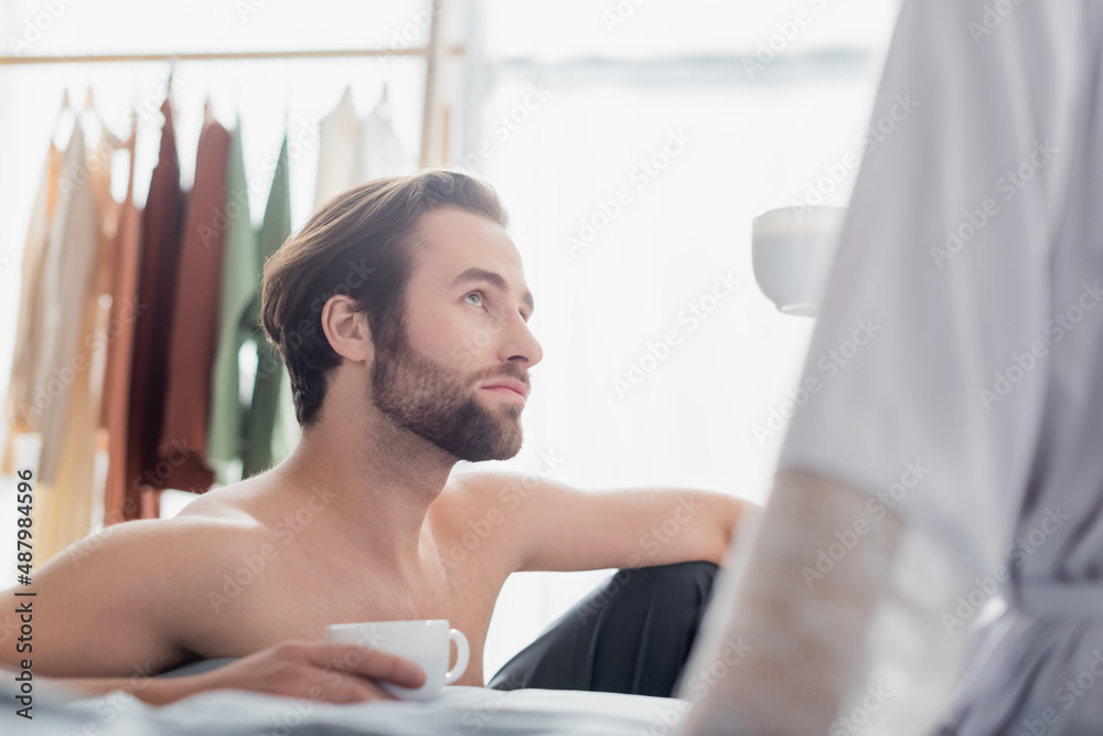 bearded man looking at woman in robe and holding cup.
