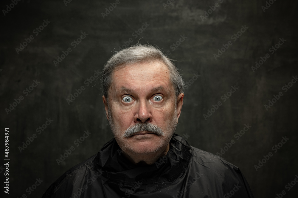 Portrait of shocked senior man looking at camera with wide eyes isolated on dark vintage background. Concept of emotions, fashion, beauty, self-reinvention