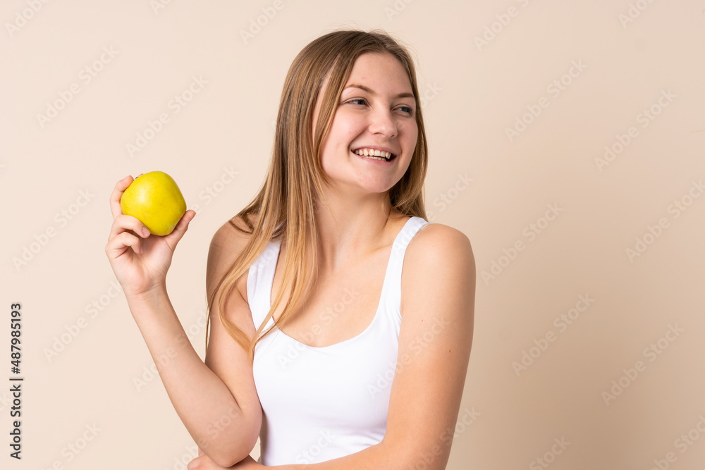 Teenager Ukrainian girl isolated on beige background with an apple and happy Teenager Ukrainian girl isolated on beige background with an apple and happy