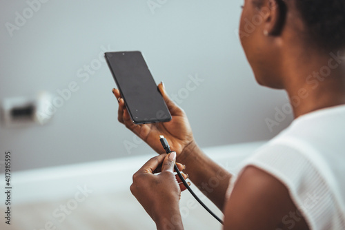 Woman hands connected charger to smart phone at home. Woman hands plugging a charger on a smart phone. Woman hands charging battery in mobile smart phone photo