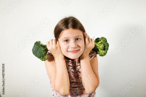 Funny kid girl with broccoli on a light background, vegetables and vitamins for children