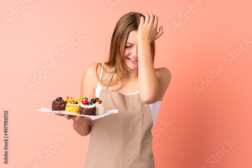 Pastry Ukrainian chef holding a muffins isolated on pink background having doubts with confuse face expression