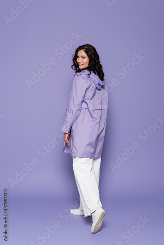 full length of cheerful young woman in violet raincoat on purple.