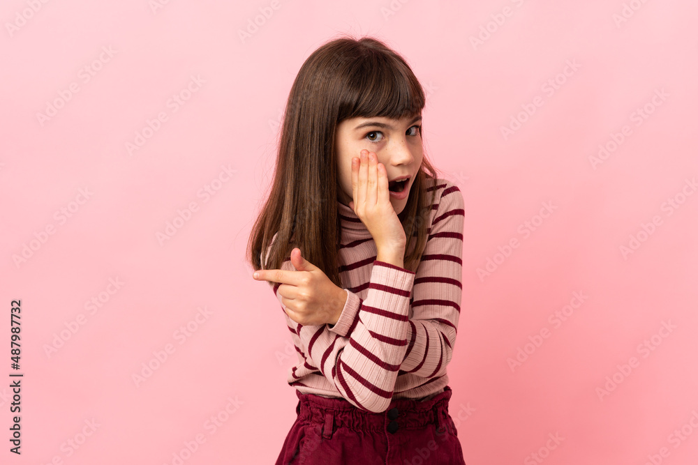 Little girl isolated on pink background pointing to the side to present a product and whispering something Little girl isolated on pink background pointing to the side to present a product and whispering something