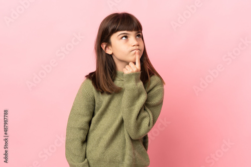 Little girl isolated on pink background having doubts while looking up © luismolinero
